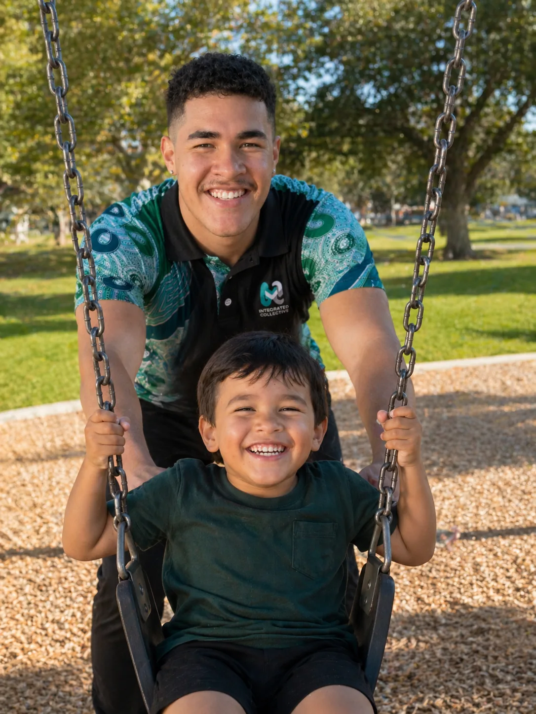 Integrated Collective youth worker pushing a smiling child on a park swing